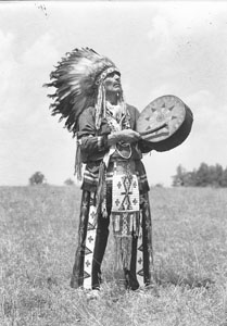 Chief Eagle Feather standing beating tom-tom held in air