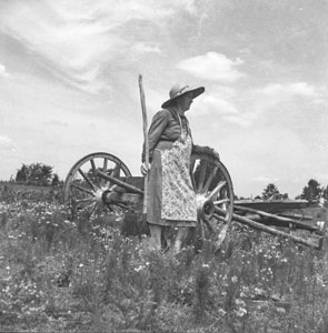 Country woman in field leaning against wagon wheel - Aunt Minnie